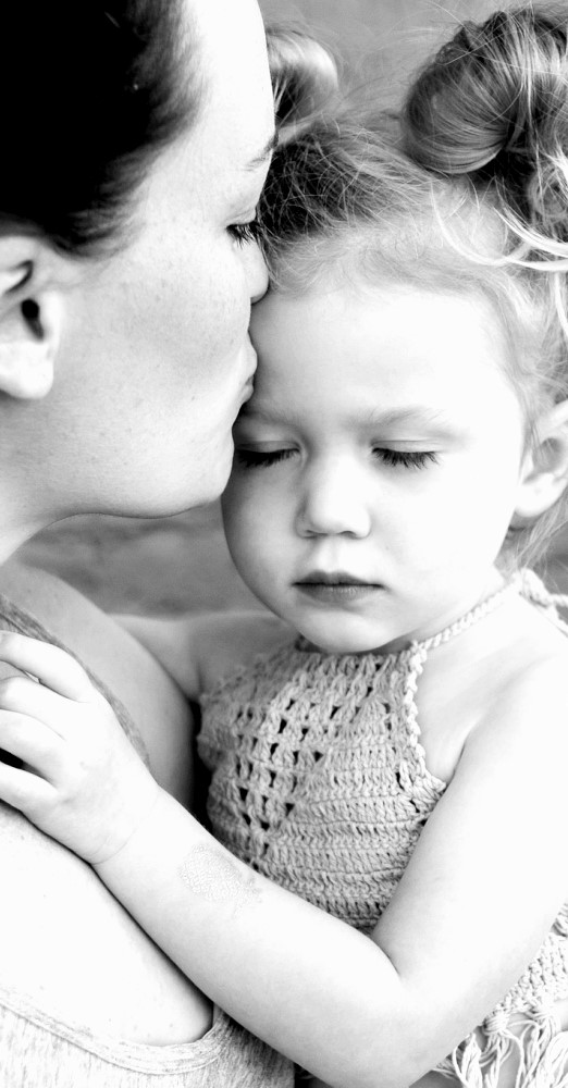 Mutter küsst Tochter liebevoll auf die Stirn